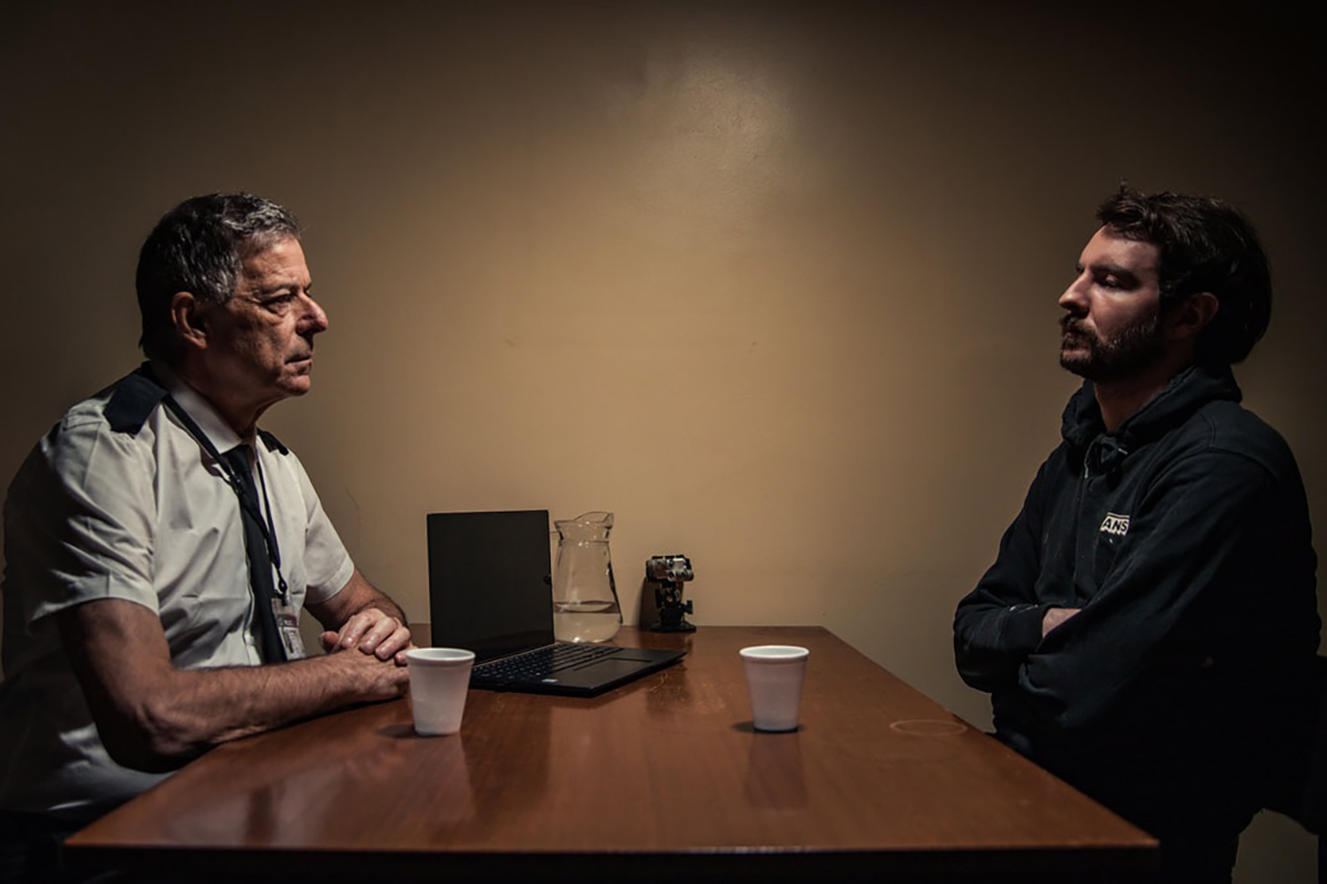 screenshot from The Trick Room - two men facing each other in police cell.